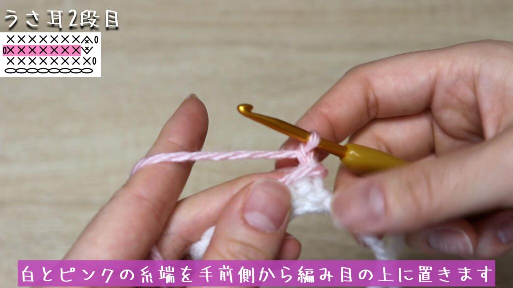 白とピンクの糸端を手前側から編み目の上に置きます